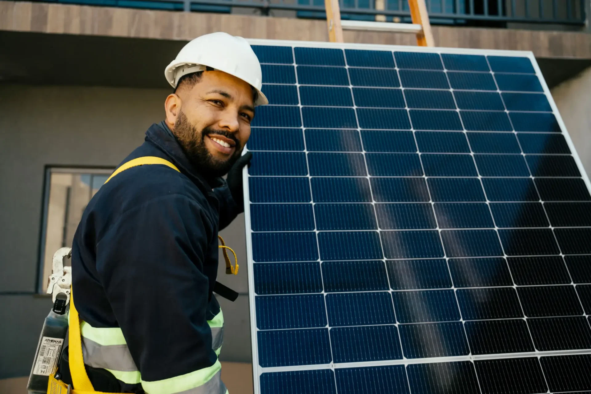 Smiling worker in safety gear installs solar panels outdoors.