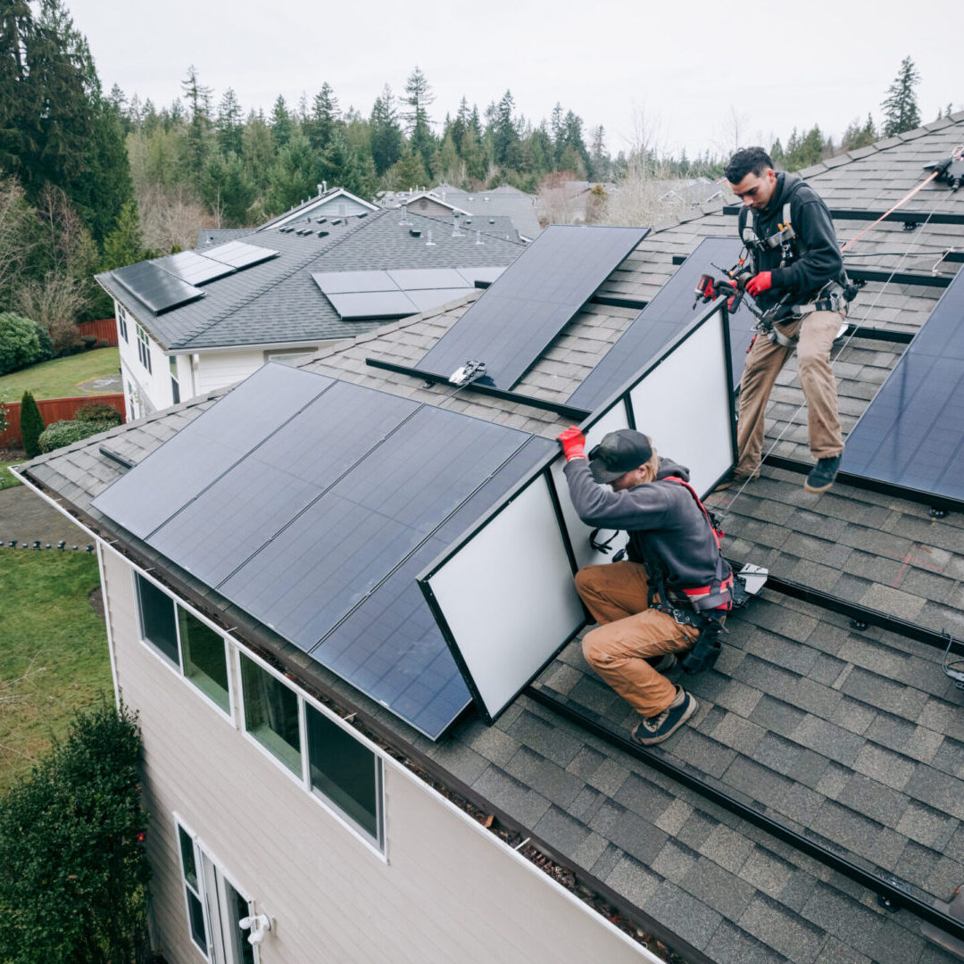 Two workers installing solar panels on a residential rooftop.